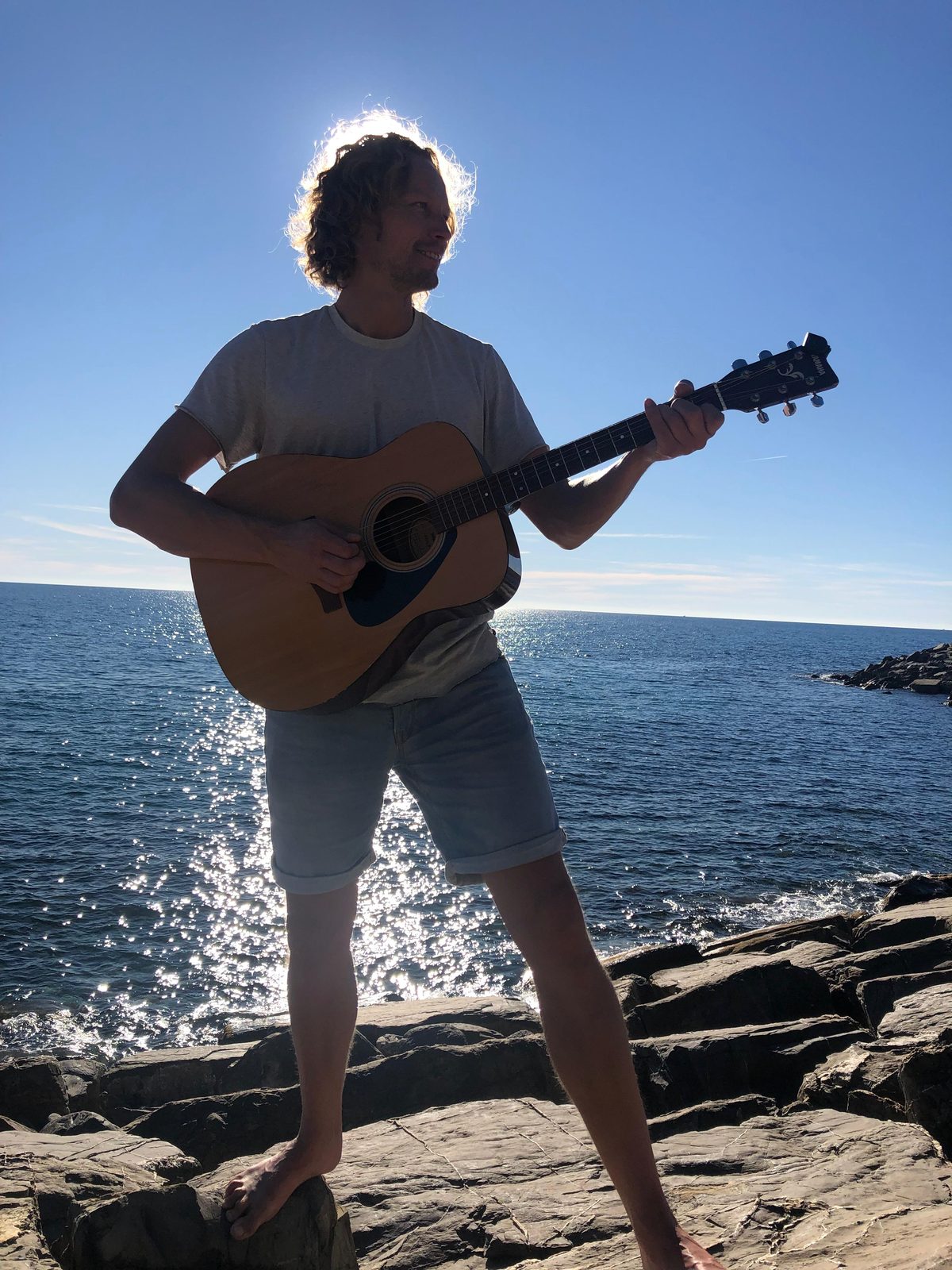 Tobi Sonic barfuß auf Felsen am Meer, im Gegenlicht